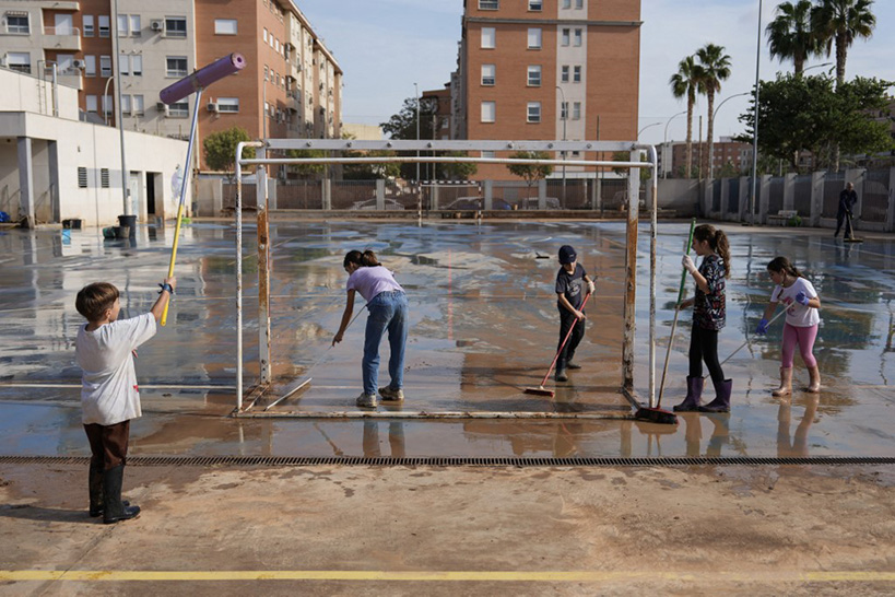 Sur cette photo prise le 5 novembre 2024, des enfants nettoient la boue et l'eau qui ont inondé leur cour de récré.